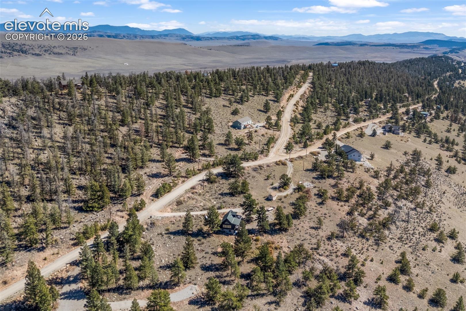 Elevated hillside acreage featuring natural coniferous landscape, unpaved road access, and expansive mountain terrain