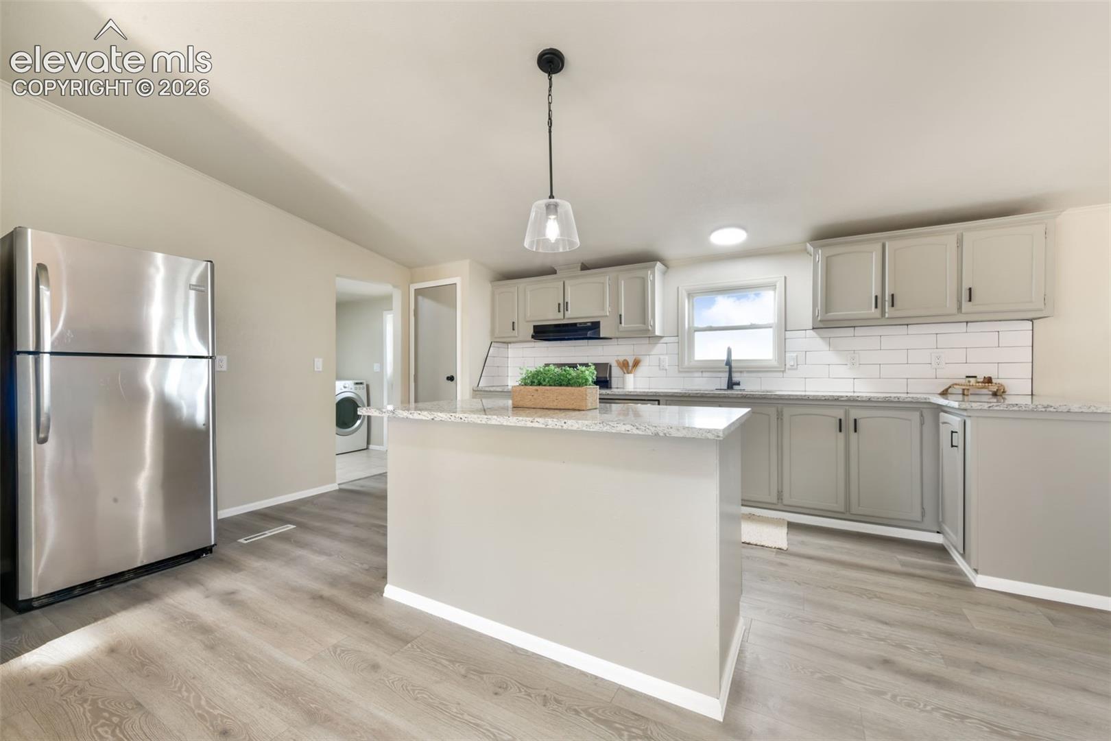 Kitchen featuring a center island, light gray cabinetry, stainless steel refrigerator, white subway tile backsplash, and wood-finish flooring