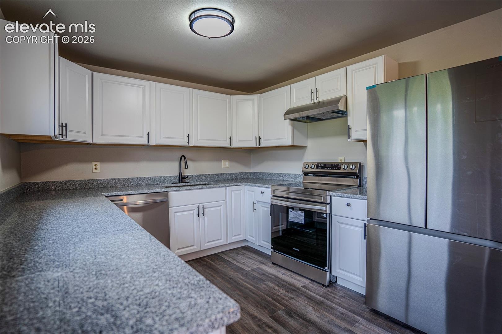 Kitchen featuring white shaker-style cabinetry, stone-finish countertops, stainless steel appliances, matte black plumbing fixtures, and wood-finish flooring