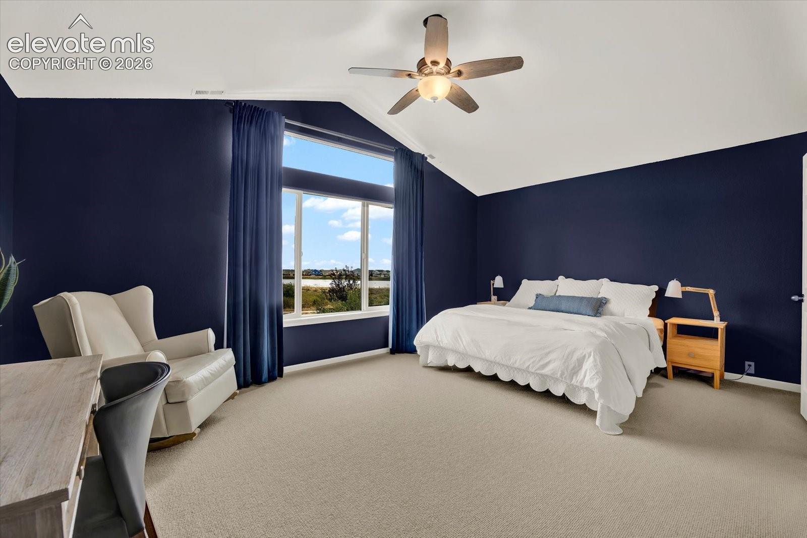 Vaulted ceiling featuring a central multi-blade ceiling fan with integrated lighting, large windows with transom, and carpeting