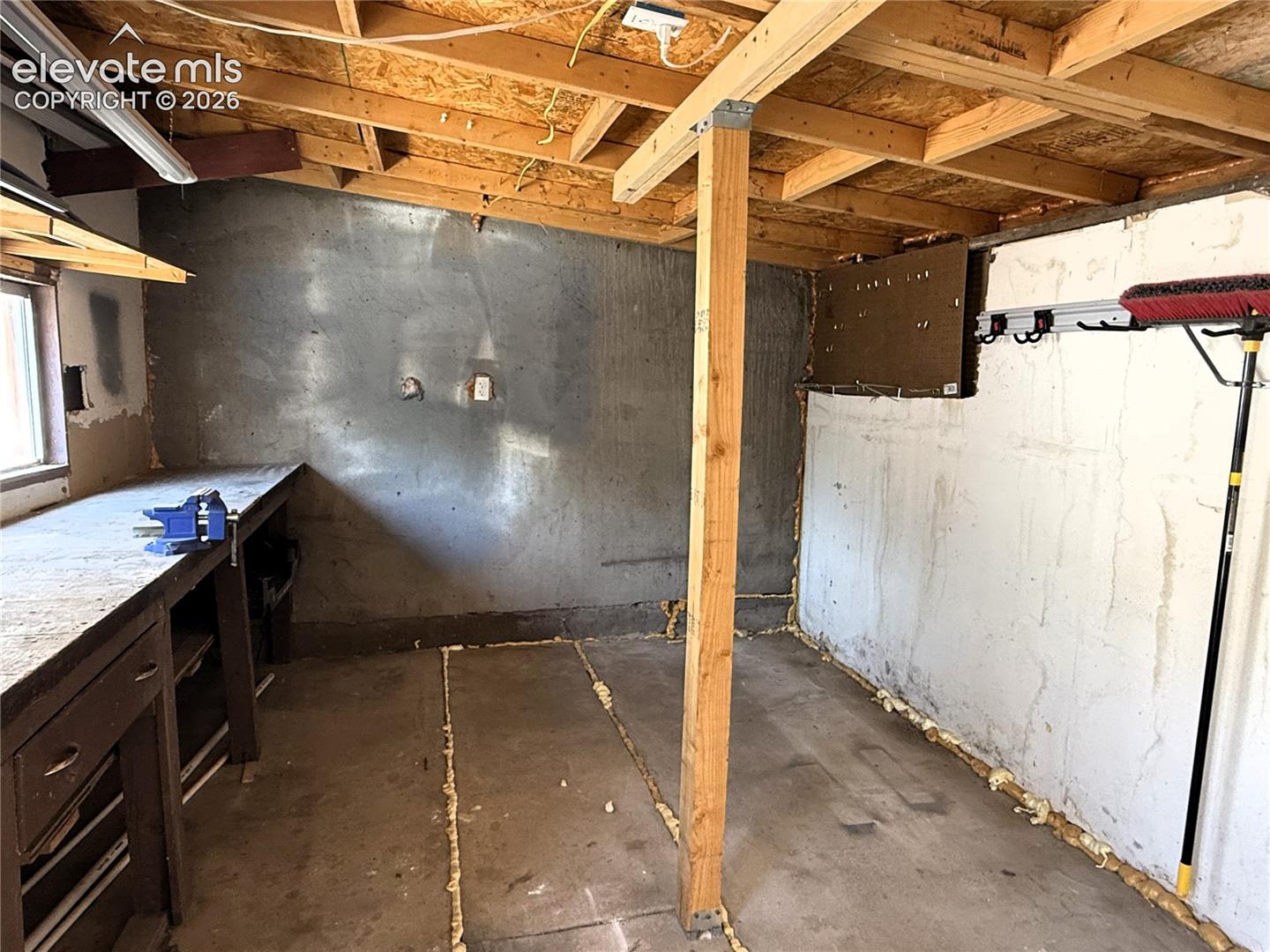 Workshop area featuring exposed wood rafters, concrete flooring, a built-in wooden workbench, and an integrated support beam