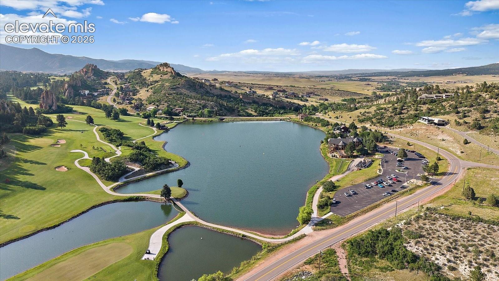 Aerial perspective featuring a large lake, surrounding mountainous terrain, sprawling golf course fairways, and paved parking areas