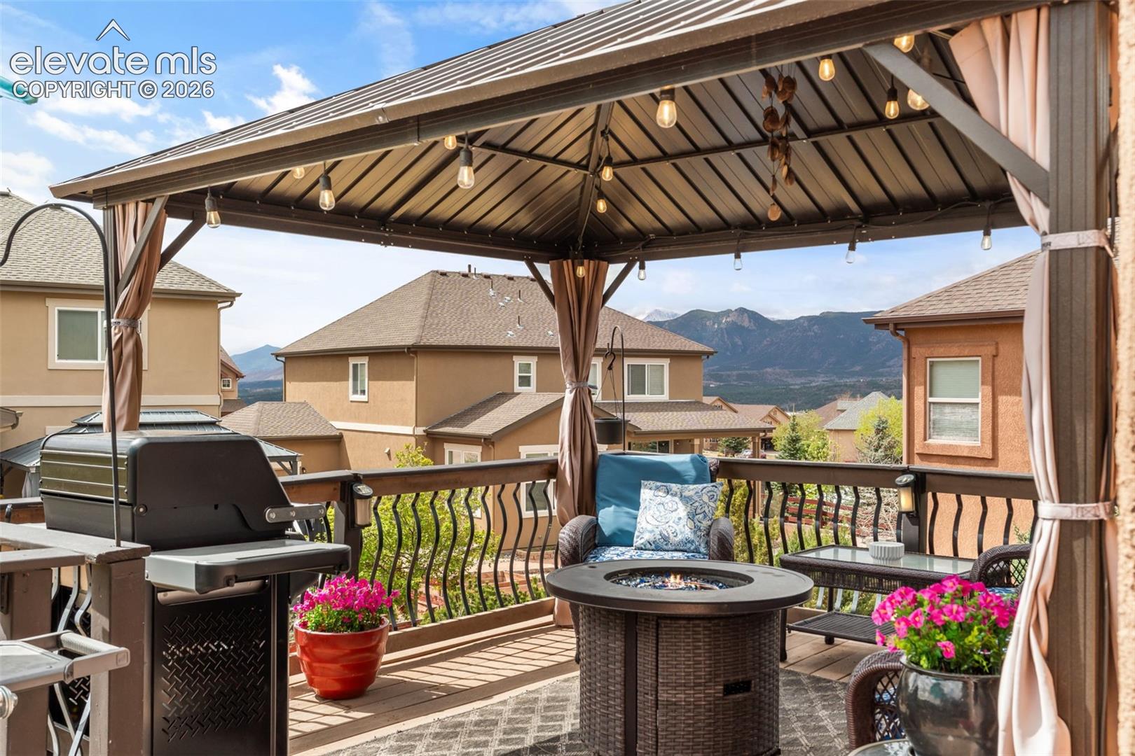 Outdoor deck featuring a metal gazebo with string lighting, a brown wood-finish railing with black metal balusters, and a mountain backdrop