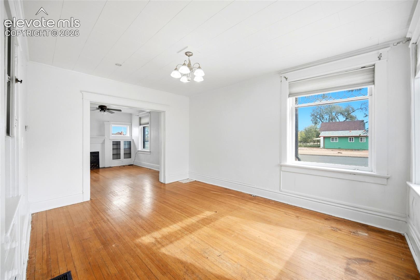 Interior space featuring natural wood-finish flooring, white plank-style ceiling, multi-light chandelier, and large window with casing trim