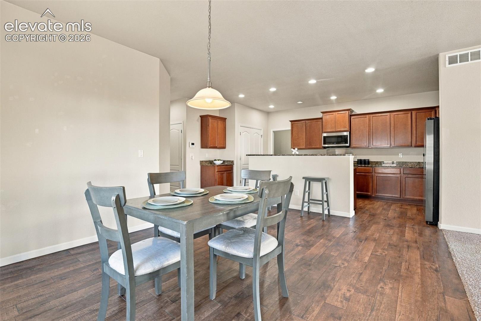 Wood-finish flooring, shaker-style wood cabinetry, stone countertops, recessed lighting, and a pendant light fixture