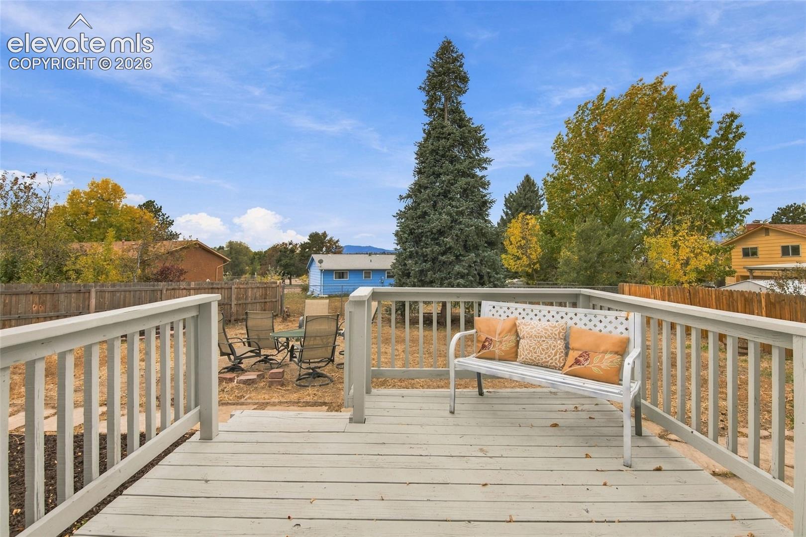 Elevated wooden deck featuring light-toned decking boards and a painted wood railing, overlooking an expansive backyard with mature trees and wood fencing