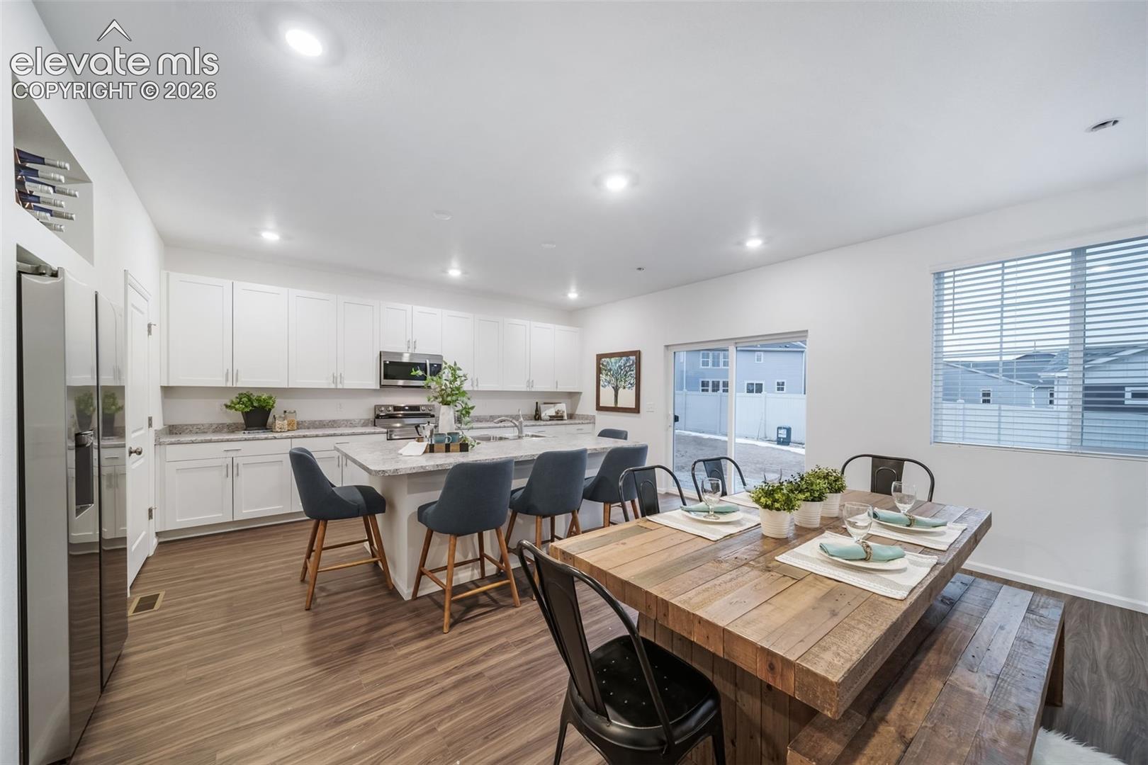 Open-concept kitchen and dining area featuring wood-finish flooring, white cabinetry, a kitchen island with seating, stainless steel appliances, and a sliding glass door
*photos of a model home*