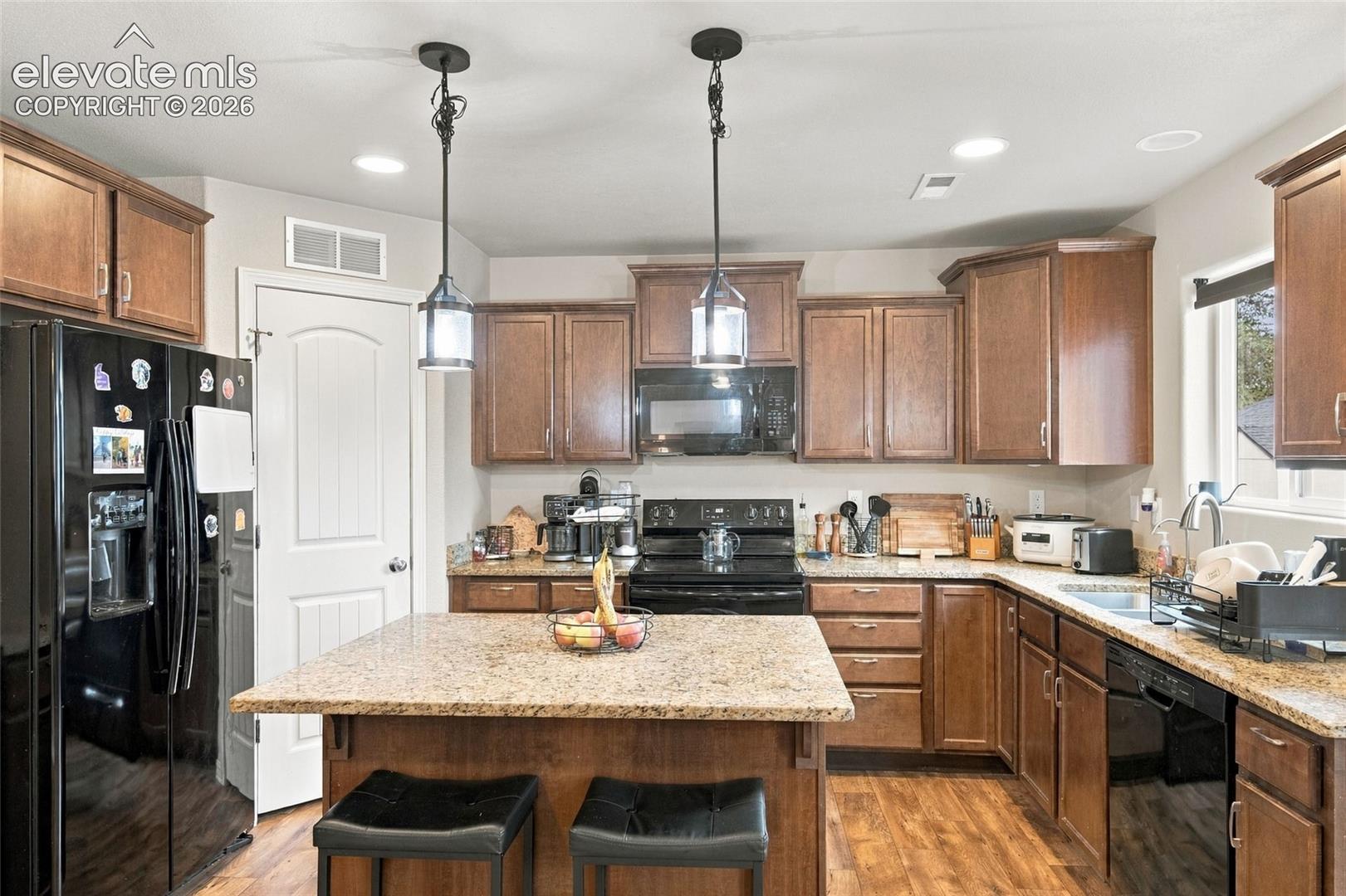 Kitchen featuring wood cabinetry, stone countertops, central island, dual pendant lighting, and wood-finish flooring