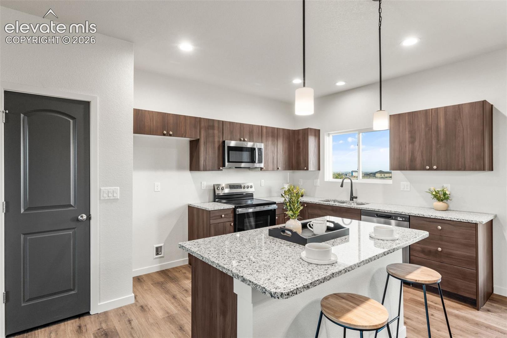 Kitchen featuring wood-finish cabinetry, stone-style countertops, an island with dual pendant lighting, wood-finish flooring, and a stainless steel built-in microwave