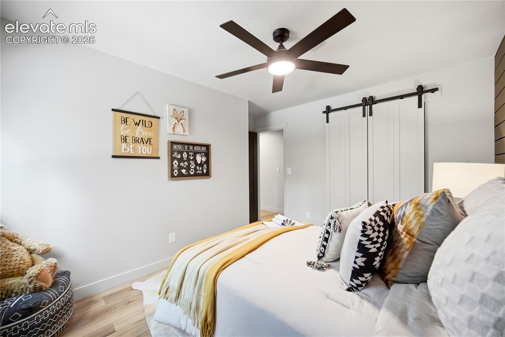 Interior room featuring wood-finish flooring, a matte black multi-blade ceiling fan with integrated lighting, and white sliding barn doors with black hardware