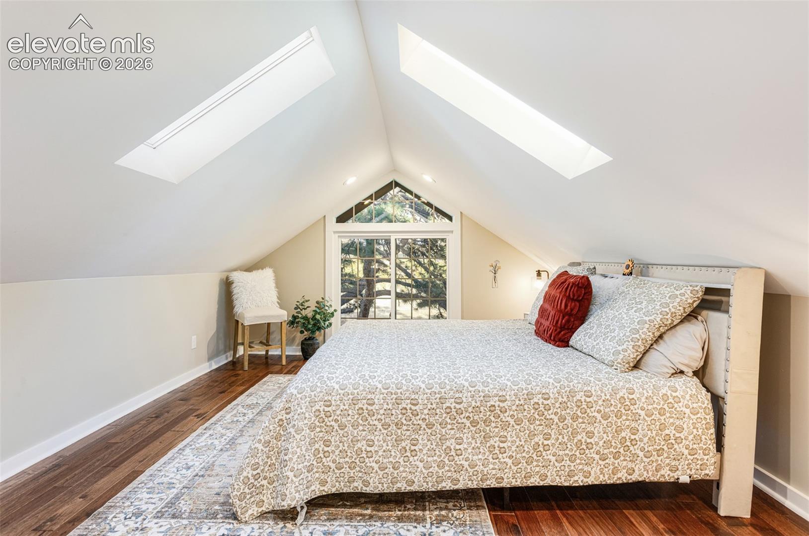 Vaulted ceiling bedroom featuring two skylights, a large picture window, recessed lighting, and wood-finish flooring