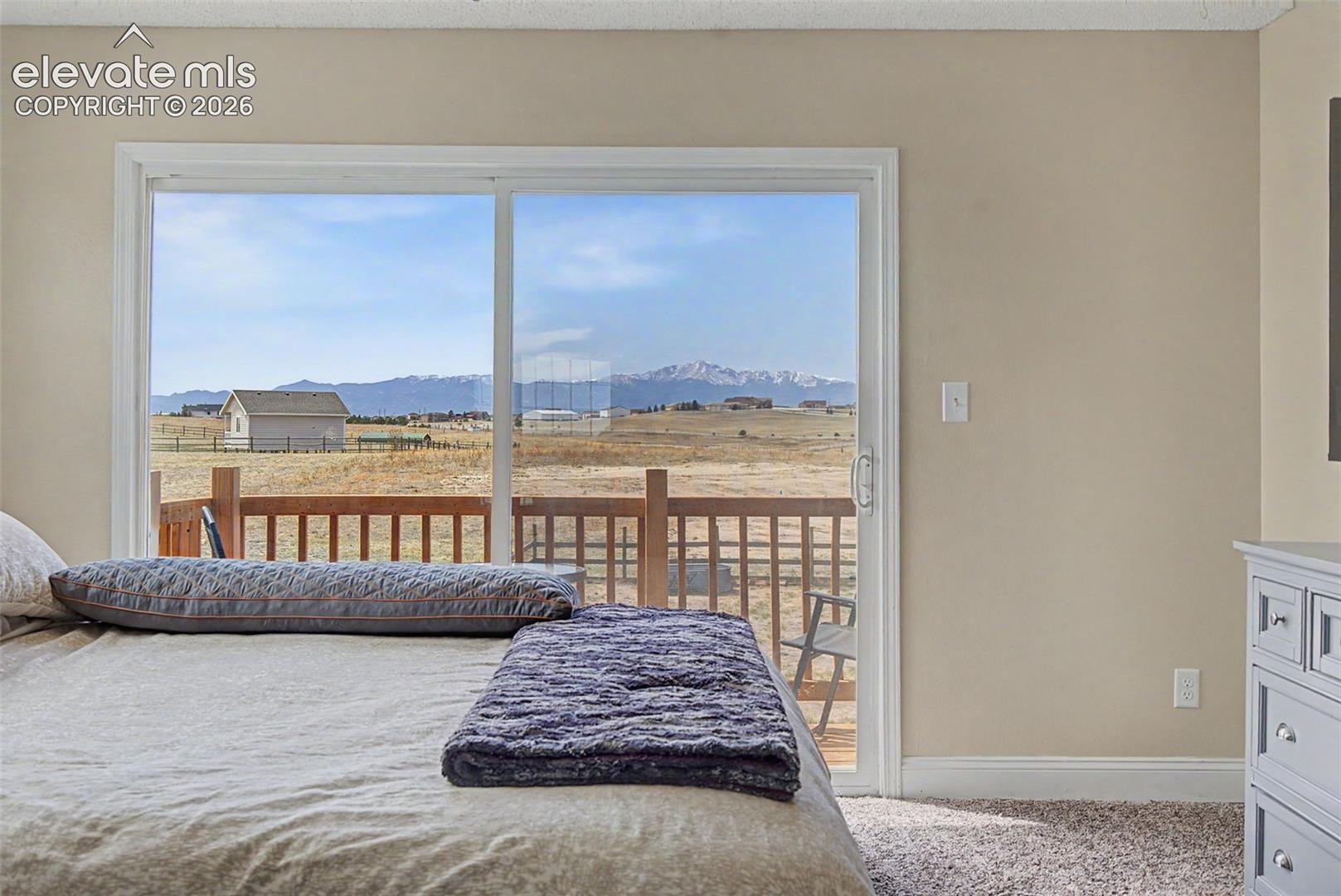 Large sliding glass door, carpeted flooring, neutral wall paint, and outdoor deck access featuring mountain scenery