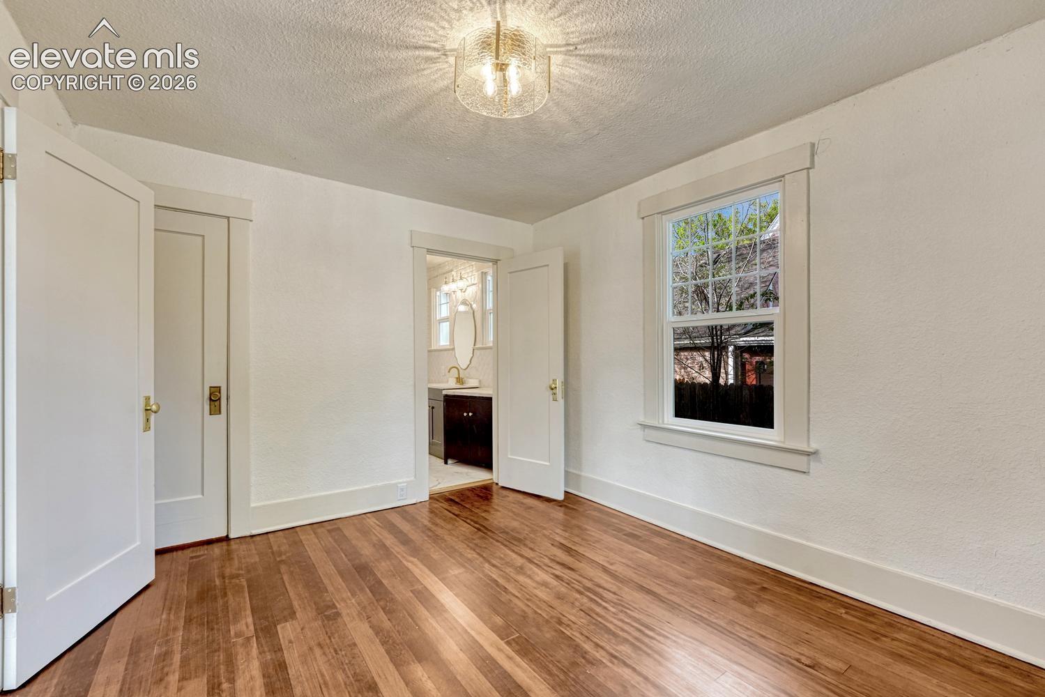 Hardwood flooring, natural light through a double-hung window, white interior doors, and a ceiling-mounted light fixture