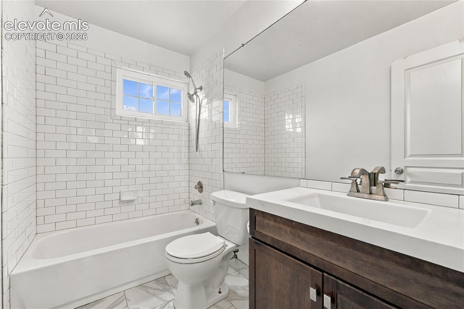 Bathroom featuring white subway tile wall surround, dark-finish wood vanity with a white countertop, integrated rectangular sink, and tile flooring