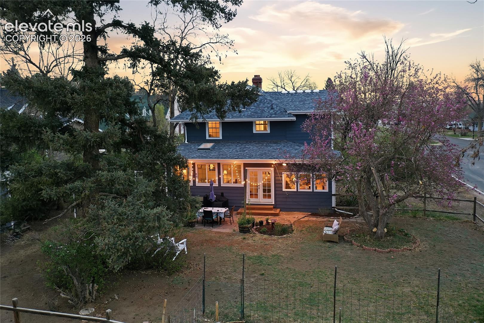 Two-story home with dark-toned horizontal siding, stone patio, multiple windows, and mature landscaping