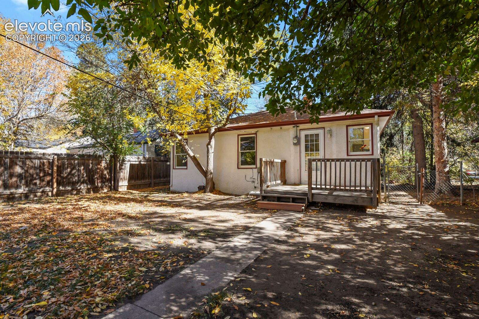 Rear exterior featuring a wood deck, light-colored stucco siding, and a fenced yard with mature trees