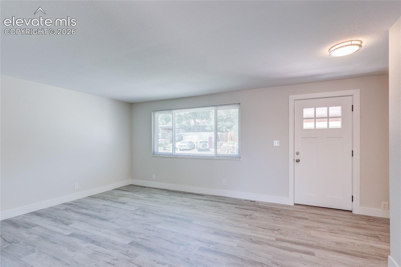 Neutral interior featuring wood-finish flooring, a large multi-pane window, and a white exterior door with glass detailing