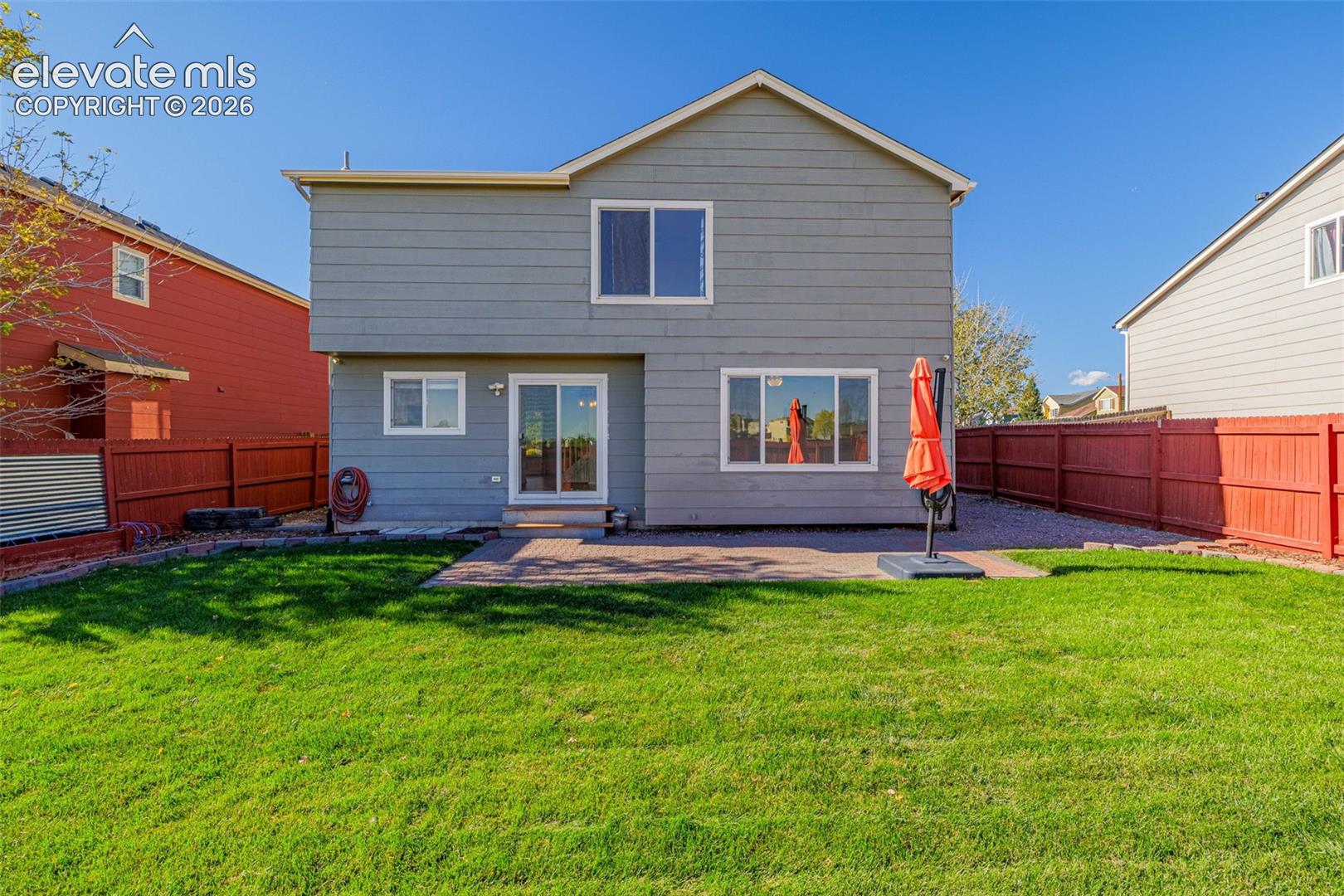 Two-story exterior with horizontal siding, rear brick-paver patio, sliding glass door, and enclosed yard with wood fencing