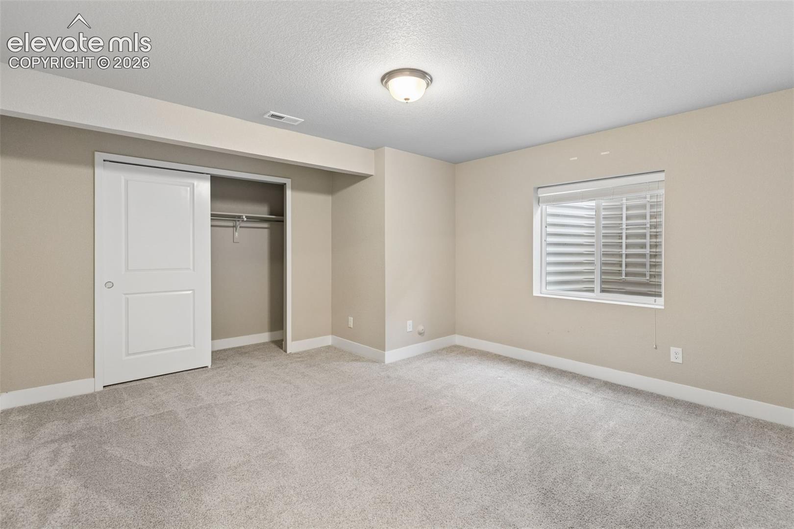 Interior space featuring neutral wall tones, wall-to-wall carpeting, an egress window, and a built-in closet with a sliding door