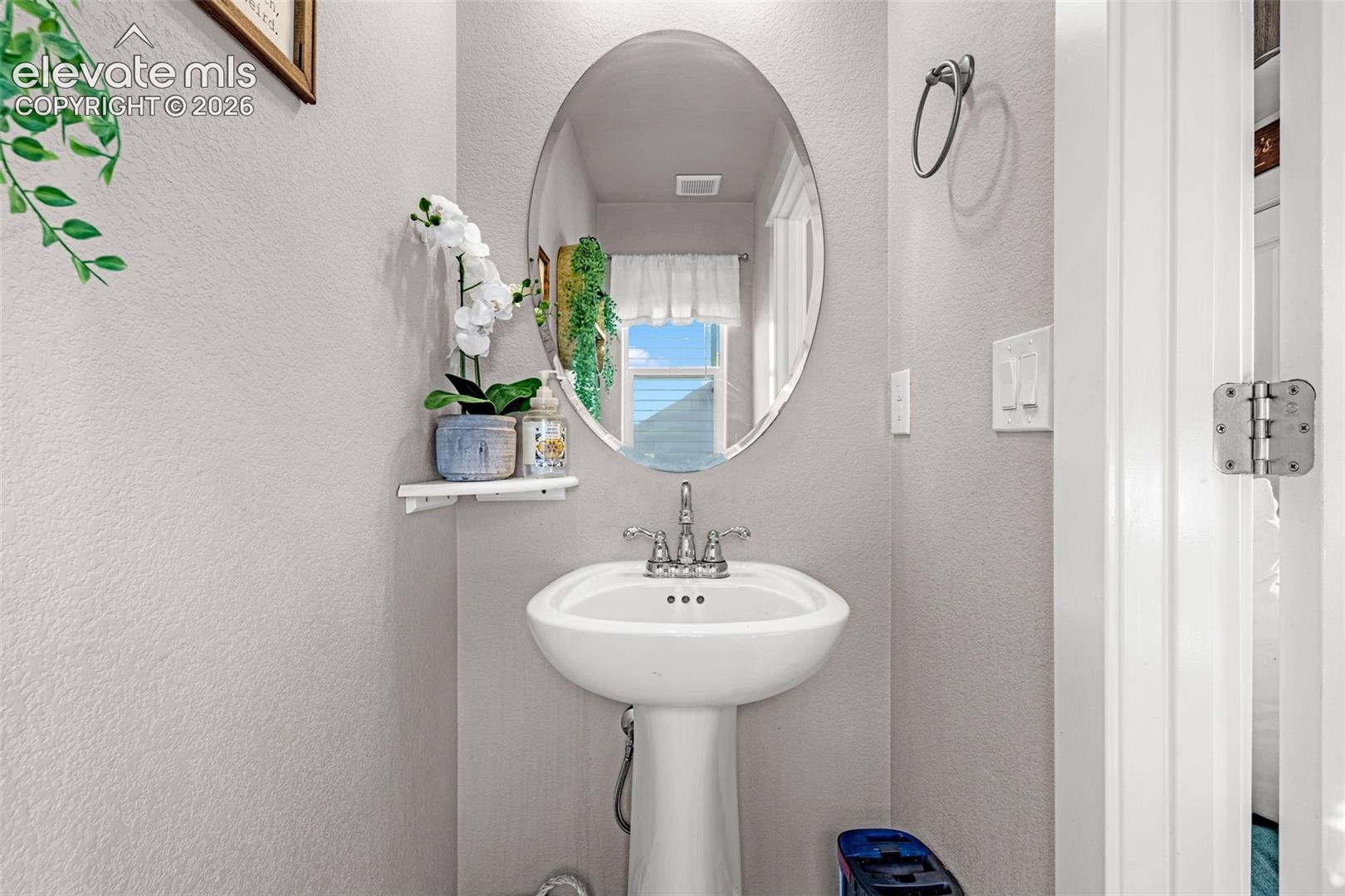 Pedestal sink with chrome faucet, complemented by an oval wall-mounted mirror