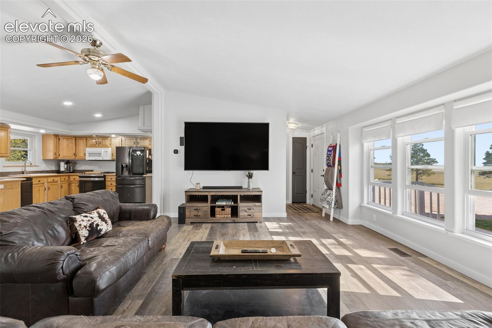 Living area featuring wood-finish flooring, vaulted ceilings with a ceiling fan, and large windows