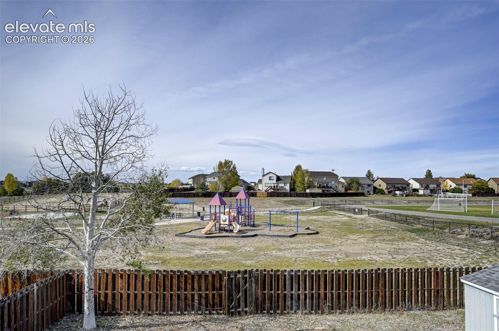Expansive open lot featuring a wood-style perimeter fence, an installed playground structure, a covered pavilion, and an open-air sports field