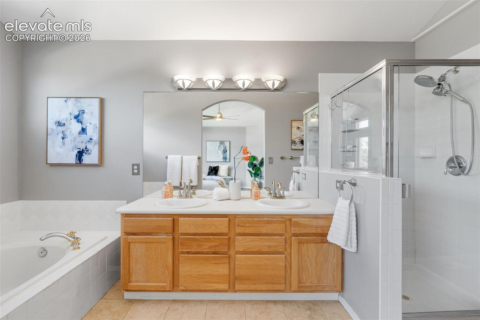 Double vanity with a composite countertop, drop-in sinks, wooden cabinetry, a full-width mirror, and a separate walk-in shower with tile surround and soaking tub