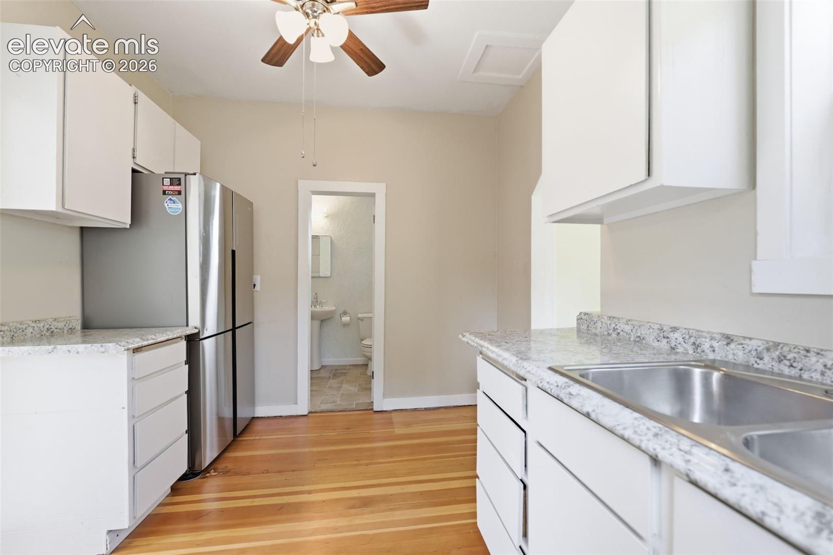 Kitchen featuring white cabinetry, a double basin sink, light-toned countertops, a ceiling fan, and pine hardwood flooring.