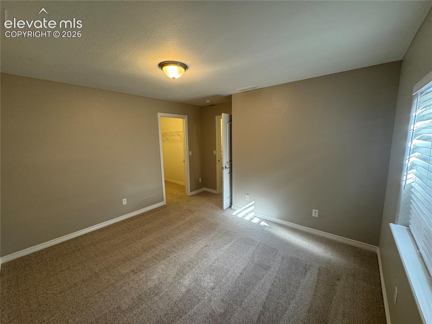 Neutral-toned interior featuring wall-to-wall carpeting, window blinds, flush-mount lighting, and dual doorways
