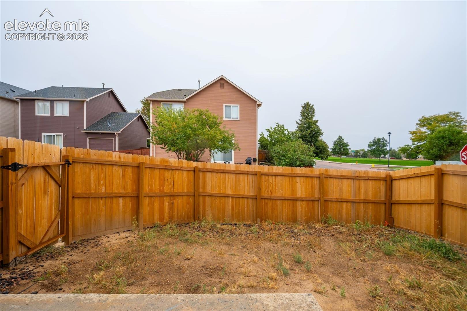 Fenced backyard with wood privacy fencing and a gate, offering direct access to an open green space