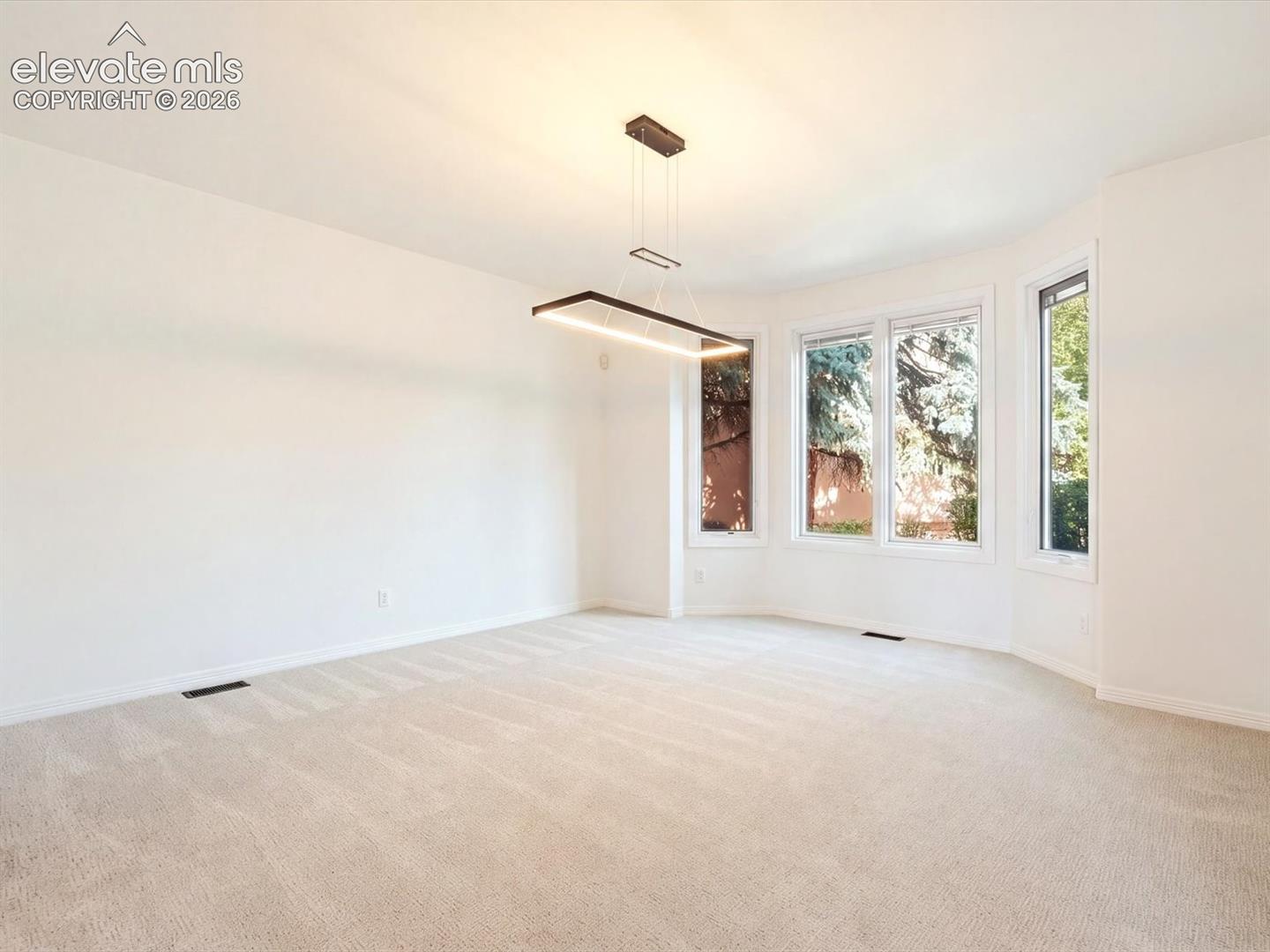 Spacious room featuring a geometric, modern pendant light fixture, wall-to-wall carpeting, and a bay window configuration