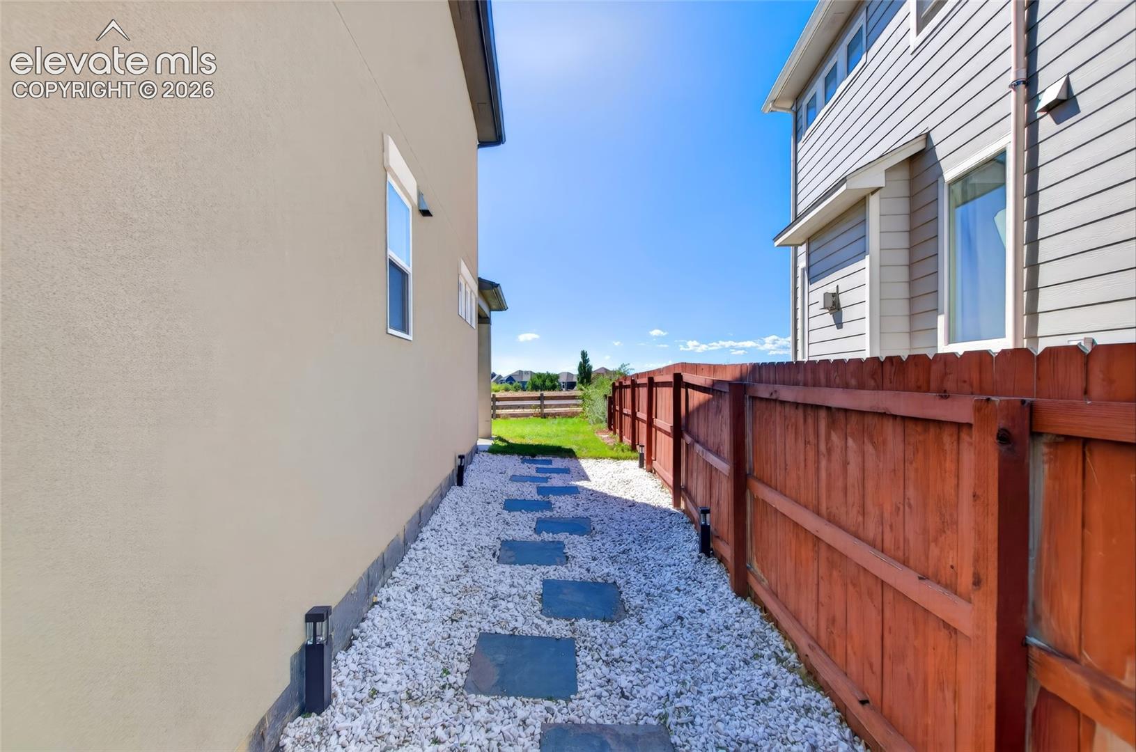 Stucco and siding exterior with a wood fence, white gravel pathway, and rectangular stepping stones