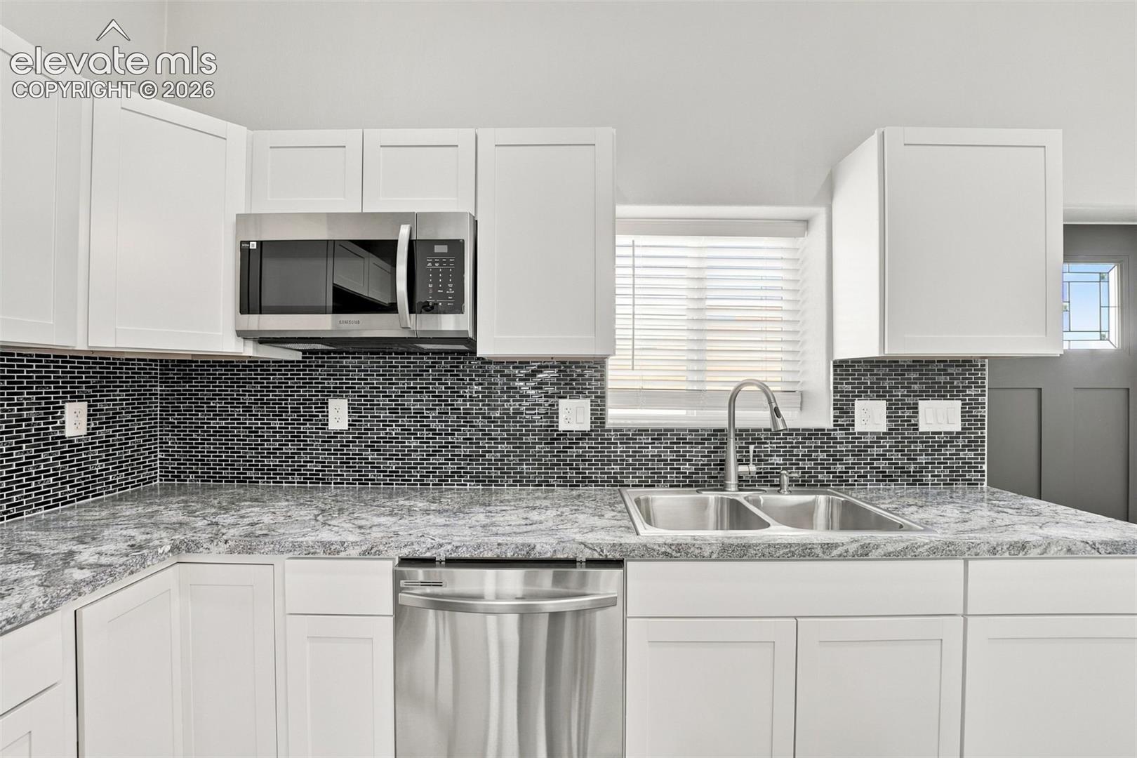 White cabinetry with stainless steel appliances, mosaic tile backsplash, and a double basin sink