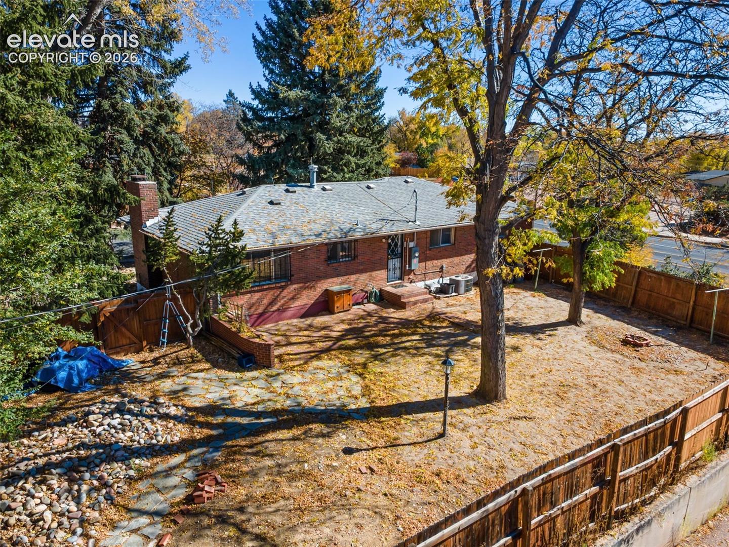 Brick exterior residence featuring a gray shingled roof, a chimney, and mature trees