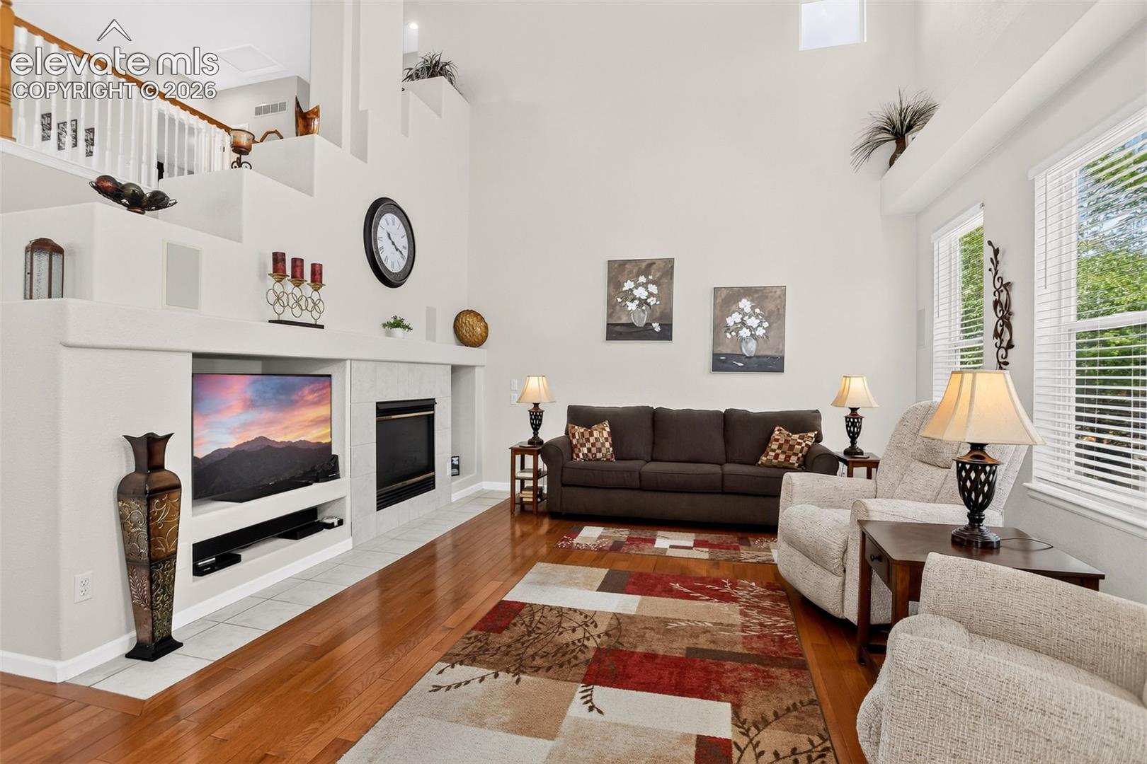 Integrated entertainment center with fireplace, hardwood flooring, large windows, and a built-in staircase
