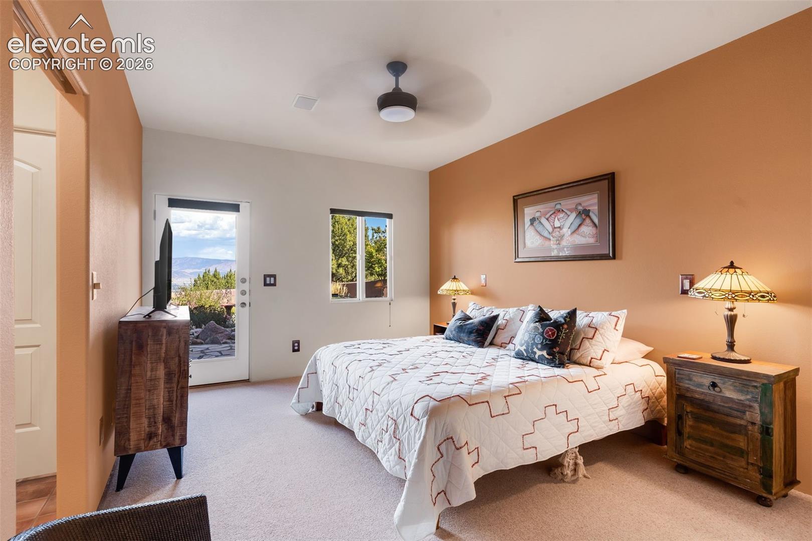 Neutral-toned carpeted flooring, glass-panel exterior door, ceiling-mounted light fixture with fan, and natural desert landscape backdrop