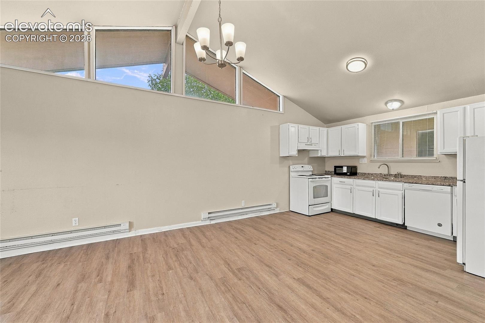 Vaulted ceiling featuring expansive clerestory windows, wood-finish flooring, white cabinetry, and multi-light chandelier