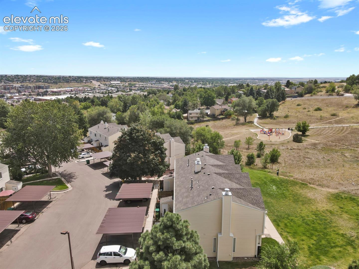Community setting featuring buildings with pitched roofs, adjacent open green spaces, and a distant urban landscape