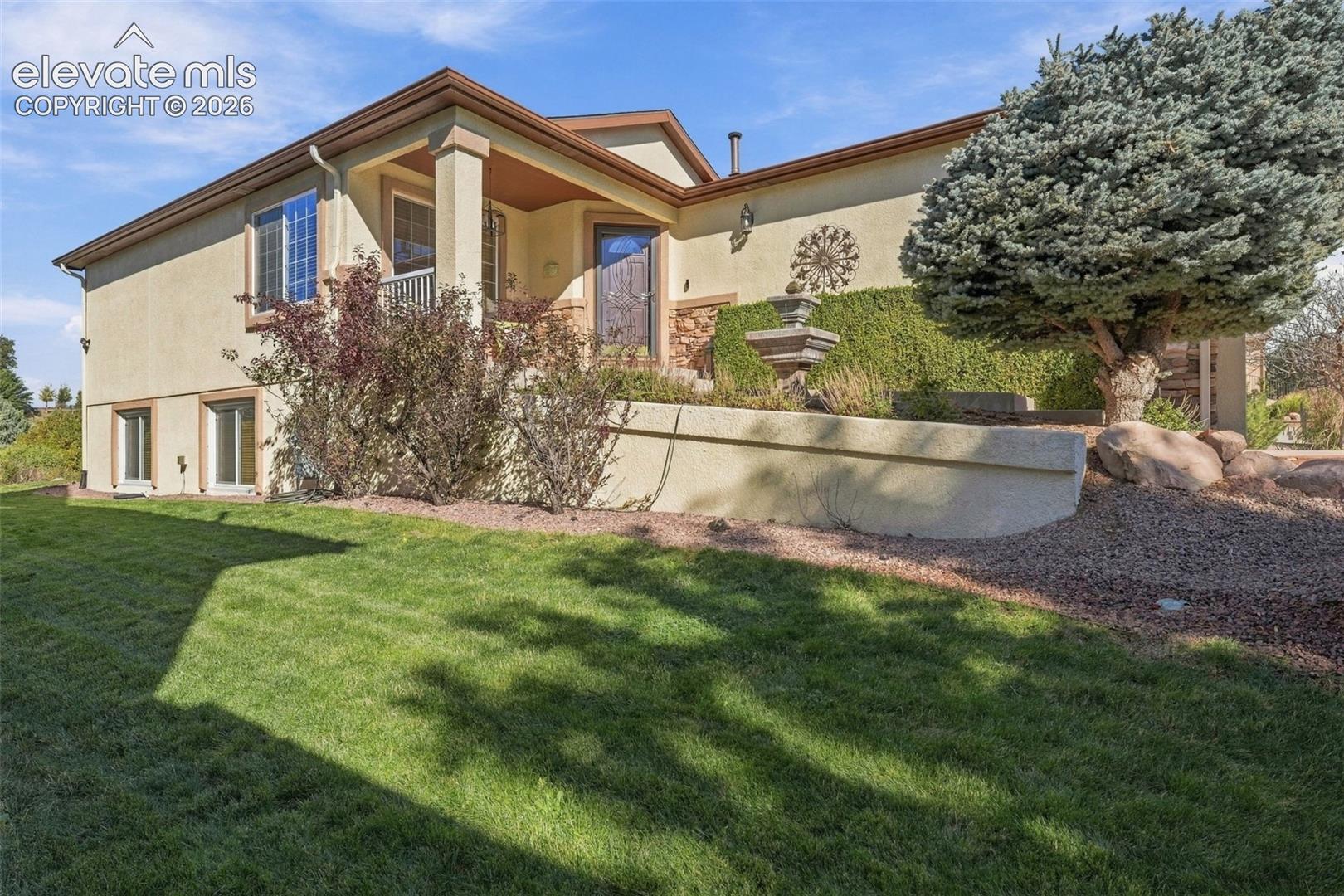 Stucco exterior featuring stone accents, a covered entrance, mature landscaping, and a built-in stone fountain
