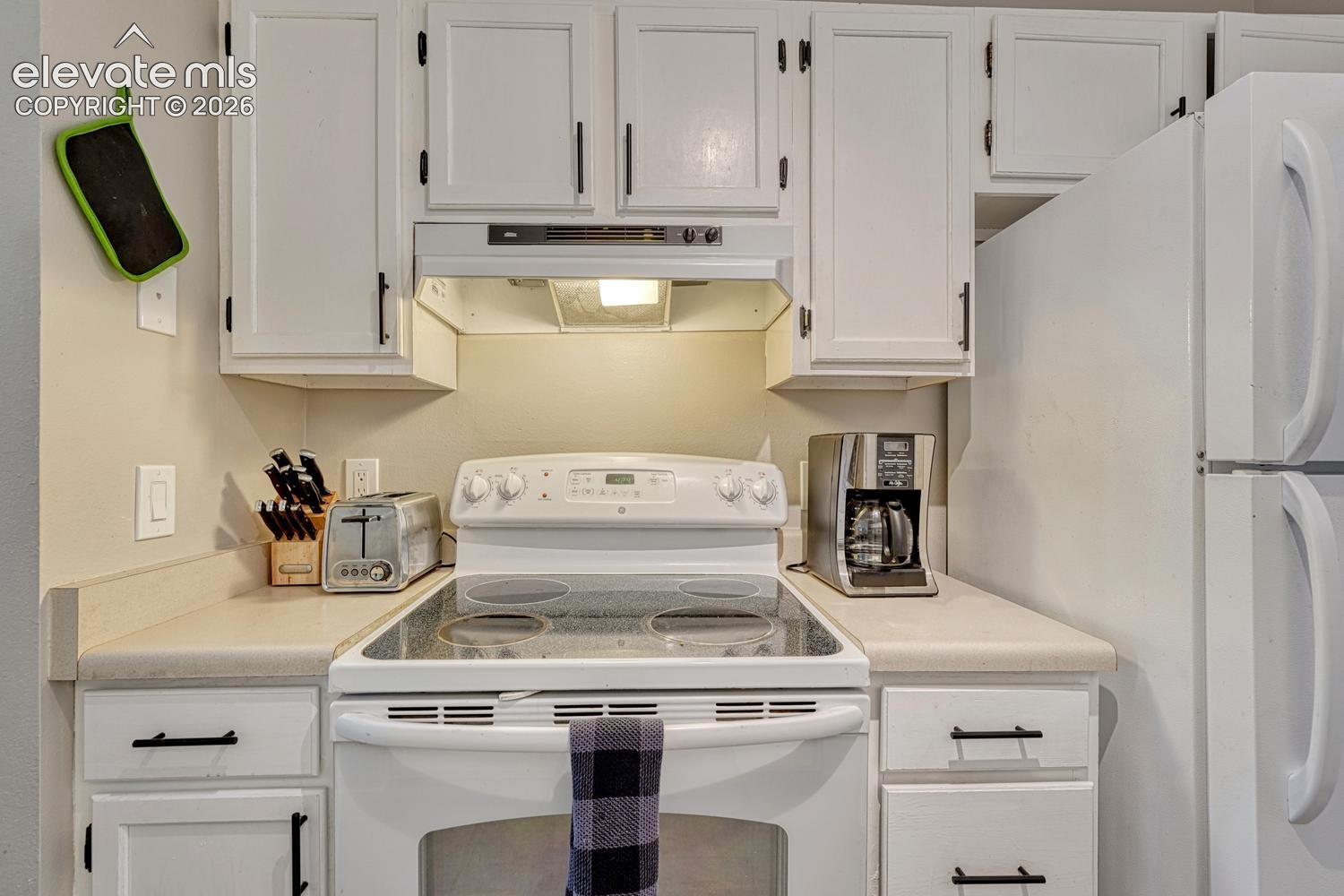 White cabinetry with black hardware, complementing white appliances, and a light-toned countertop