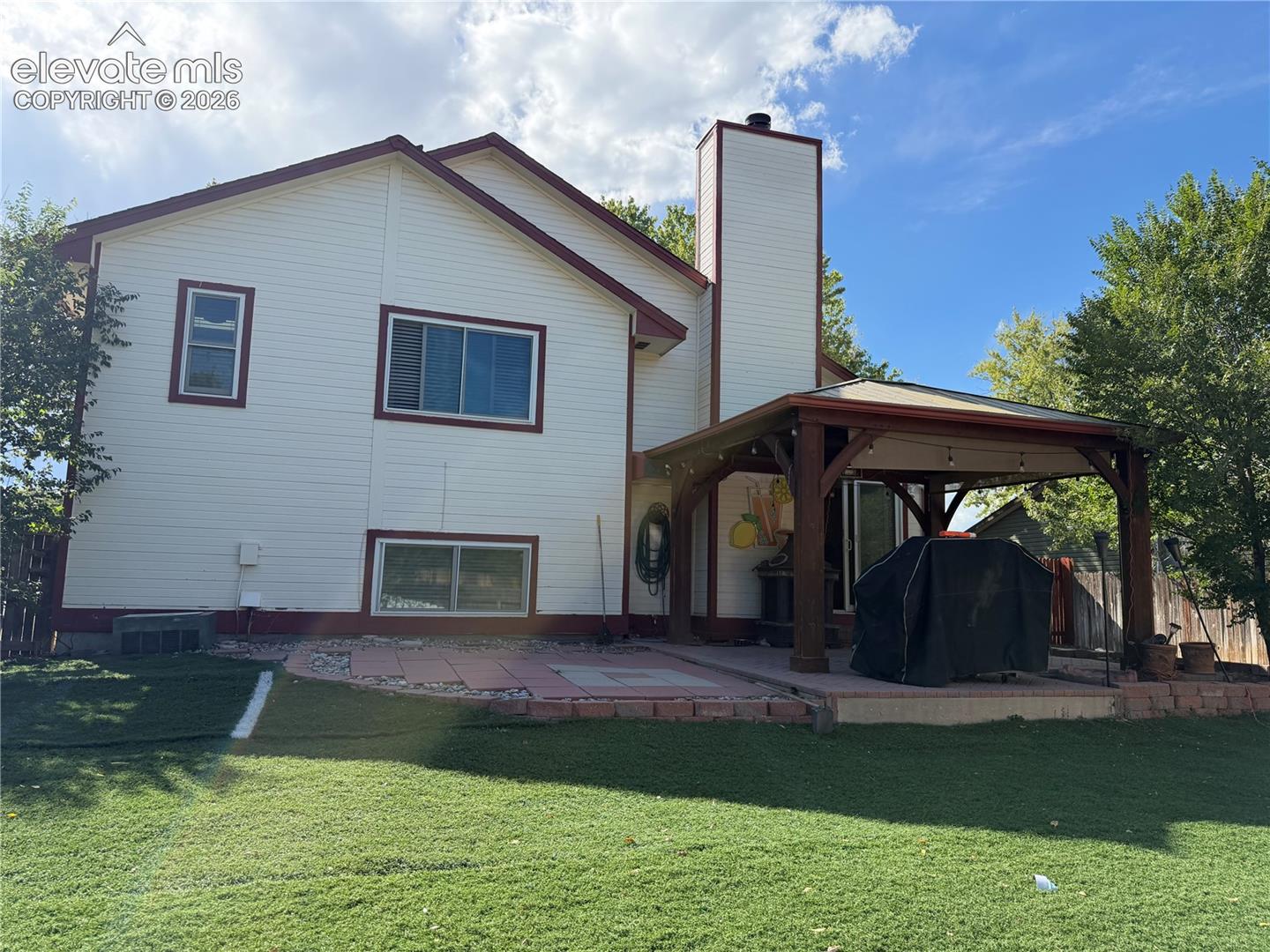 Expansive backyard featuring a large paved patio, a wood-frame covered gazebo, and a stucco chimney