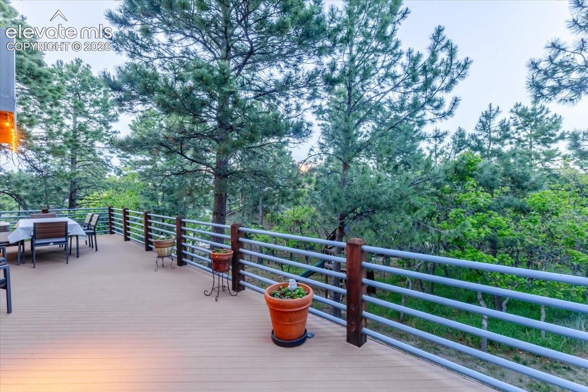 Expansive outdoor deck featuring wood-finish flooring, a metal and wood railing system, and mature evergreen trees surrounding the property