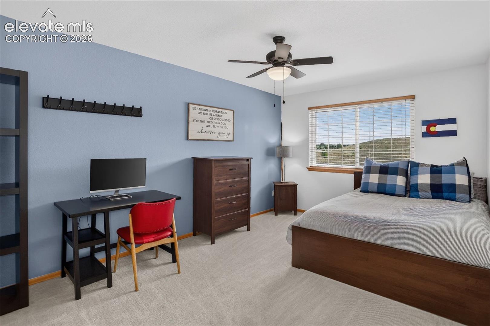 Carpeted room featuring a single window with blinds, a ceiling fan with integrated lighting, and a prominent accent wall