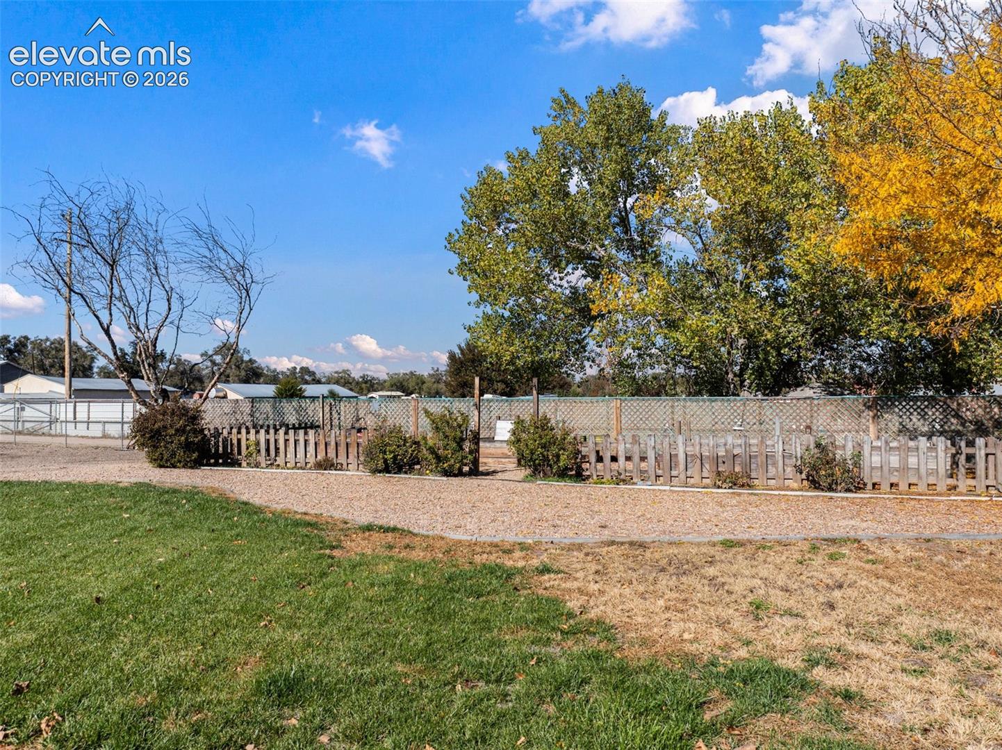 Expansive grounds featuring a gravel lot, wood picket fencing, lattice privacy screening, and mature trees