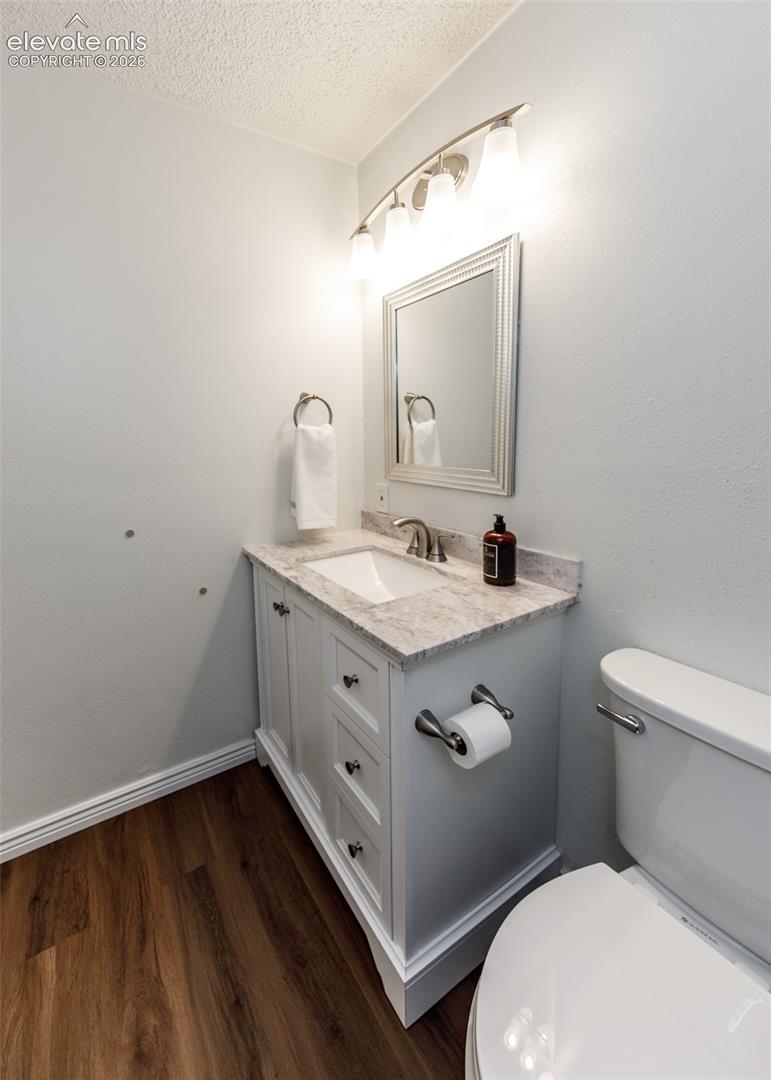 White vanity with stone-finish countertop, integrated basin, brushed-metal hardware, and wood-finish flooring