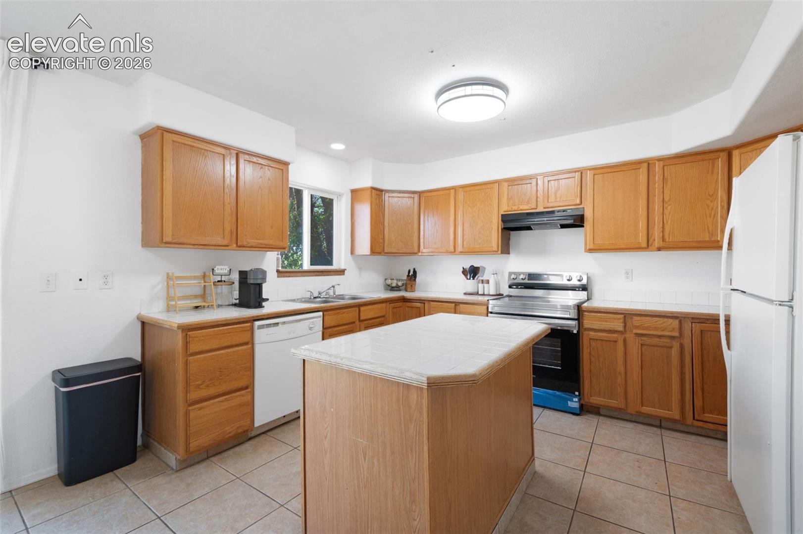 Kitchen with wood-finish cabinetry, tile flooring, and a central island with a light-toned countertop