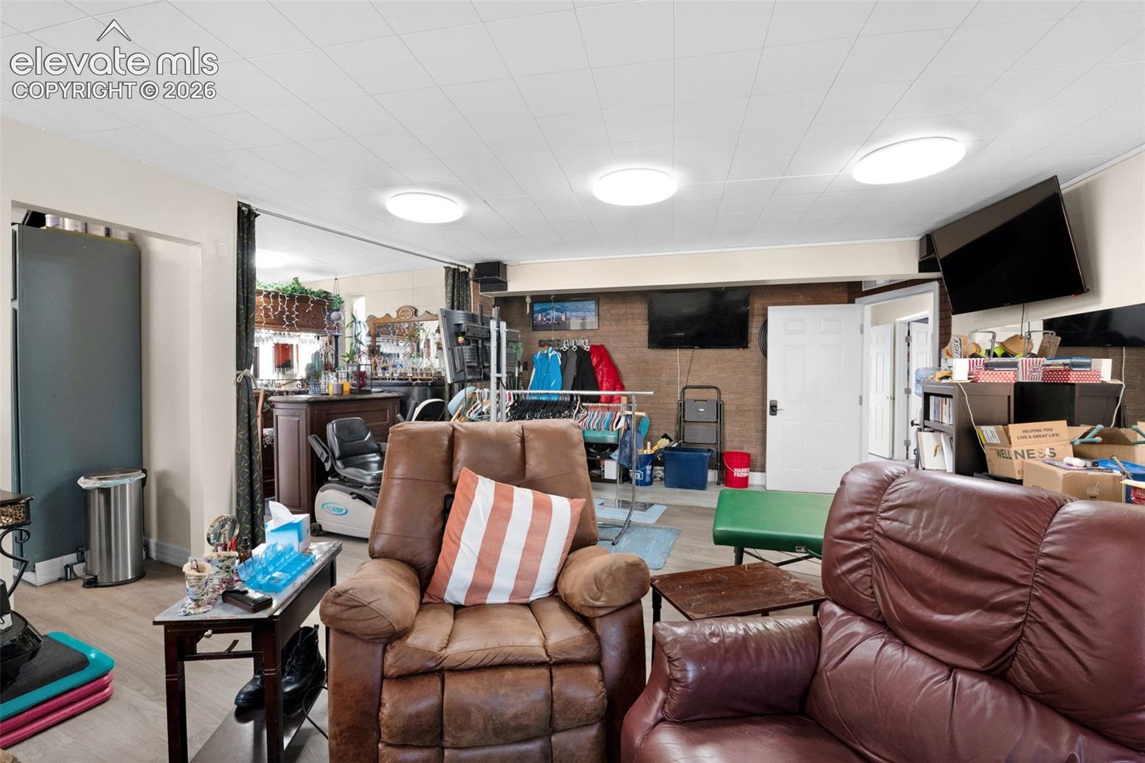 Open-concept interior featuring wood-finish flooring, exposed brick wall accents, and multiple flush-mount ceiling light fixtures
