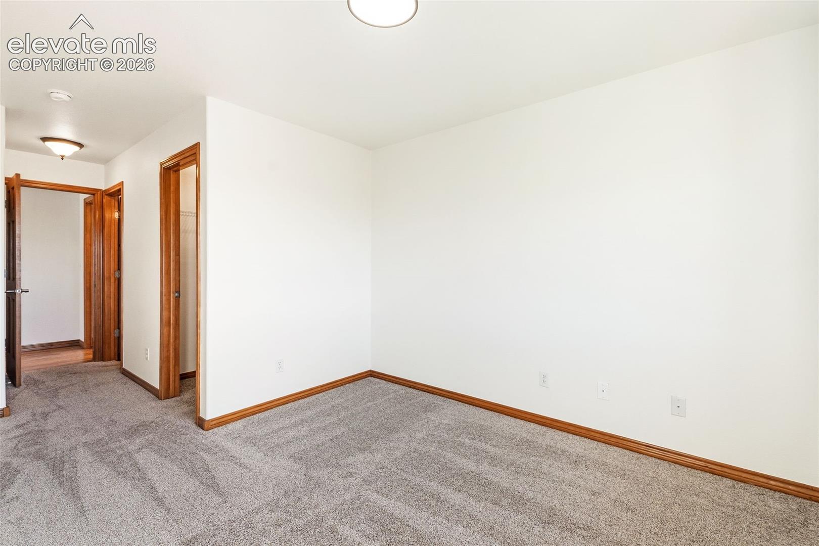 Neutral wall tones, carpeted flooring, and wooden door trim featuring a flush-mount overhead light fixture