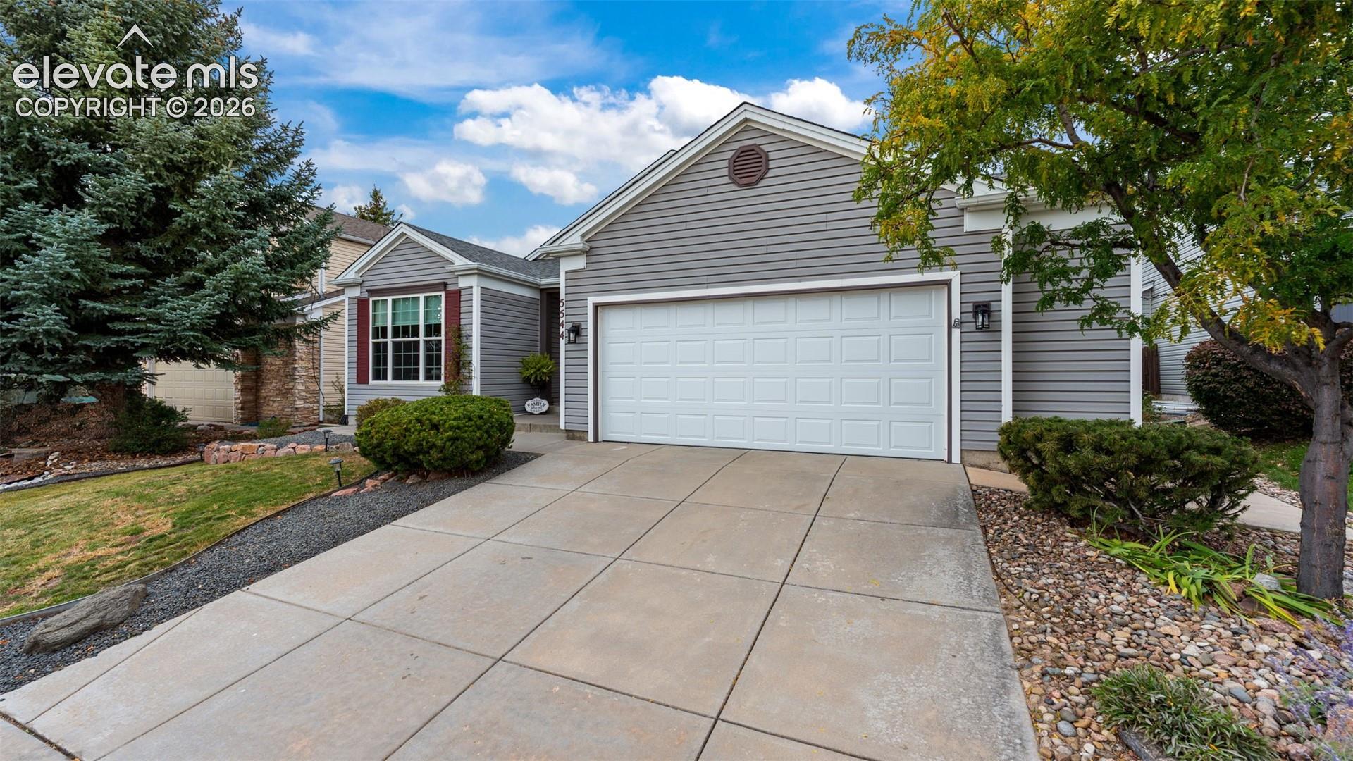 Exterior featuring gray horizontal siding, a two-car garage with a paneled door, stone accent wall, and mature landscaping