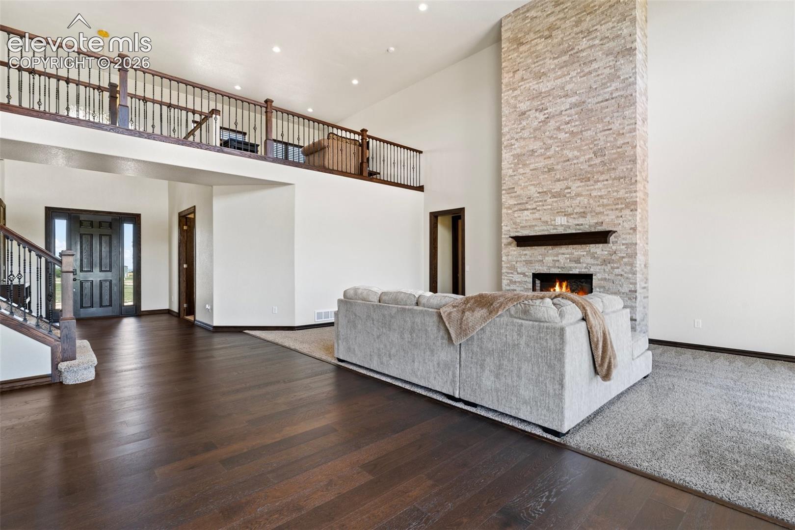 Great room featuring a floor-to-ceiling stone fireplace with a dark wood mantel, high ceilings, recessed lighting, and dark wood-finish flooring